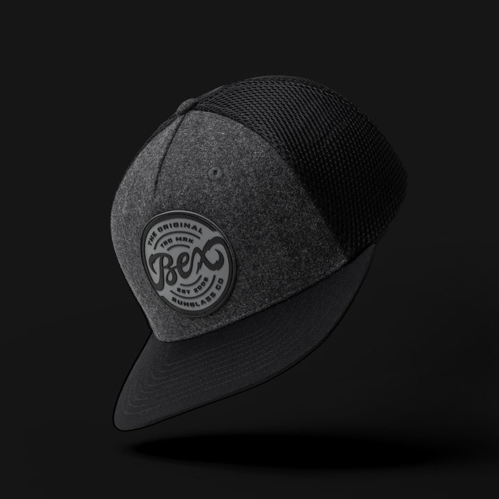 Flat bill trucker cap in dark grey melton wool and black spacer mesh back completed with a black suede under visor #color-gray-black
